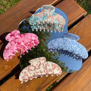 Detailed view of colorful large acetate hair claws on a mirror with outdoor reflections