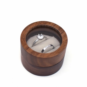 Top view of a round walnut wood wedding ring box with a clear window showing two rings