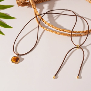 Detail of adjustable brown cord necklace with golden slider and resin square pendant