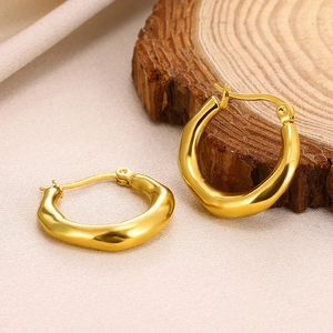 Detailed side view of golden irregular wavy hoop earrings on a natural wood surface