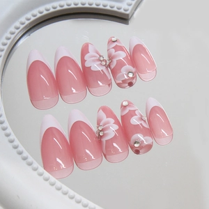 French almond press-on nails with pink floral designs and crystals on a mirror tray