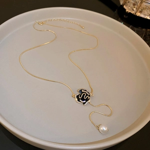 Detail of gold necklace with black enamel floral pendant and white round pearl drop