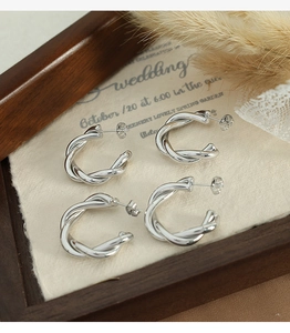 Detailed view of silver twisted C-shaped hoop earrings on vintage paper background