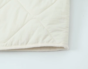 Macro view of cream quilted cotton jacket showing herringbone tape binding and stitching
