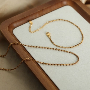 Collar minimalista de cuentas doradas con piedras marrones en bandeja de terciopelo