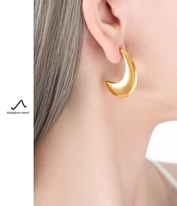 Gros plan d'un mannequin portant des boucles d'oreilles lune en acier doré à l'oreille