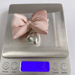 Pink satin bow keychain with silver heart charm on a scale showing 12.1g weight