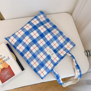 Minimalist blue and white plaid canvas tote bag with red pinstripes on a white desk