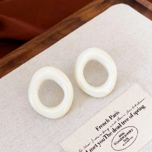 Detailed close-up of cream-colored irregular geometric resin earrings on wood