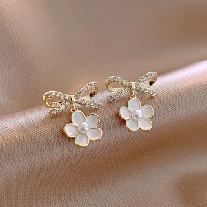 Close-up of golden bow flower earrings with pearls on elegant champagne silk fabric