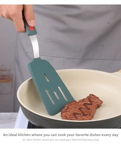 Detail of dark green silicone spatula with stainless steel handle frying steak in a pan