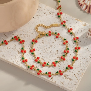 Golden cherry necklace and bracelet set on beige marble background for a summer look