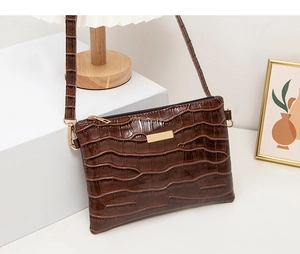 Detail of brown crocodile pattern crossbody bag with golden hardware and leather texture