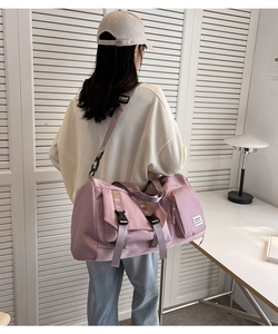 Pink travel duffle bag with reinforced black buckles and side pocket shown on a model