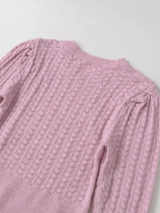 Close-up detail of pink knit sweater showing hollow wave pattern and ribbed crew neck