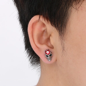 Close-up of a punk style skull stud earring with a red gemstone on a person's ear