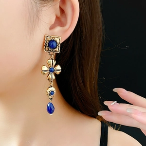 Detail of vintage gold earrings with blue gemstones and drop pendants on model