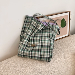 Detail view of a plaid tote bag with green and white patterns on a textured surface