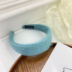 Detail of light blue fuzzy knitted headband with a hand made woven label on wood tray