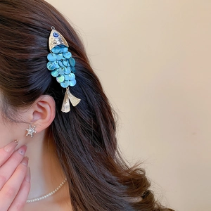 Detailed view of a fish-shaped shell hair clip with iridescent scales on brown wavy hair