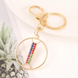 Macro shot of gold alphabet keychain with colorful rhinestones on a white ceramic tray