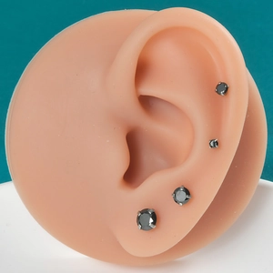 Close-up of four black cubic zirconia stud earrings in gradient sizes on an ear model