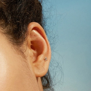 Close-up of golden sterling silver screw back stud earring with crystal on model ear