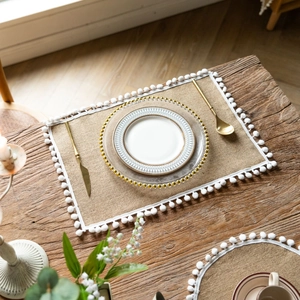 Detail of natural jute table runner featuring delicate white pom-pom lace trim on rustic wood