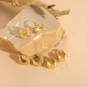 Three pairs of 14K gold plated hoop earrings with star and crescent designs on a rock