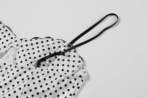 Detail of white polka dot dress featuring adjustable black straps and delicate lace trim