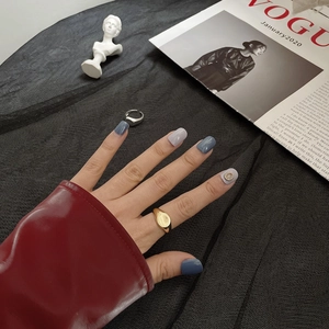 Close-up of minimalist gold ring and blue-grey nail tips against a vogue magazine background