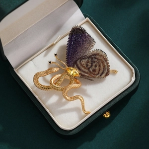 Detailed close-up of exotic snake and butterfly brooch with purple wings in a jewelry box