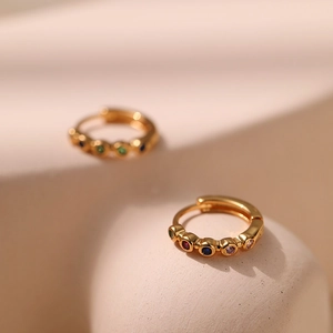 Gold huggie earrings with colorful zircon stones on a minimalist geometric background