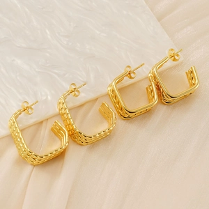 Close-up of golden multi-layered earrings with woven texture on a marble background