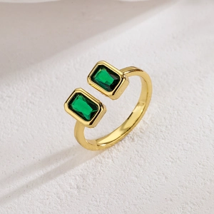 Bague ouverte géométrique dorée avec deux zircons verts sur une surface en pierre
