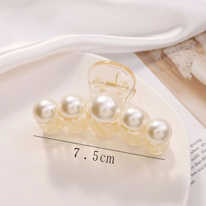 Detail view of a 7.5cm amber hair claw clip with five large white pearls on silk fabric
