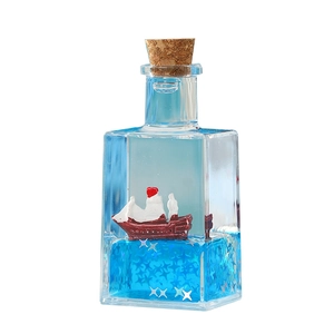 Close-up of a miniature red sailboat floating in blue liquid inside a glass bottle desk ornament