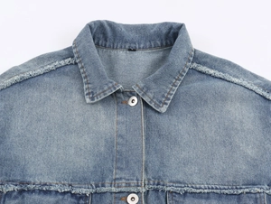 Detail view of denim jacket collar and shoulders with distressed edges and metal buttons