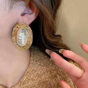 Close-up of vintage gold textured oval earrings with large pearl inlay on a model