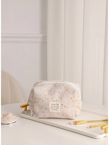 Large beige woven tweed cosmetic bag with colorful flecks on a white decorative tray