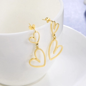 Golden stainless steel dangling earrings featuring hollow heart-shaped cutouts on ceramic