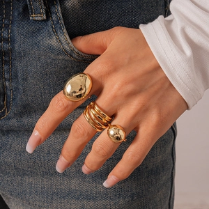 Detailed view of three chunky gold geometric rings worn on fingers with a denim background