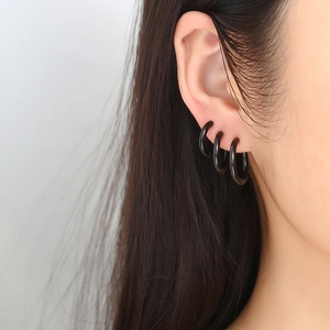 Gros plan de trois boucles d'oreilles créoles noires en acier de tailles différentes
