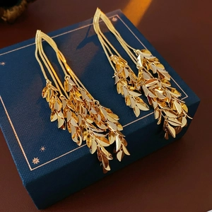 Golden leaf tassel earrings with layered chains on a blue jewelry gift box