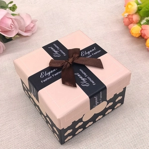 Scatola regalo quadrata rosa e nera con cuori e fiocco marrone su base di tela di iuta