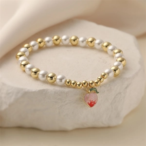 Close-up of pink peach charm on a beaded bracelet with gold beads and white pearls