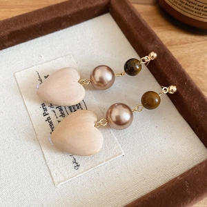 Detail view of vintage wooden heart and tiger eye stone pearl drop earrings on a tray