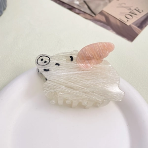 Cute pig-shaped acetate hair claw clip with pink wings on a white display plate