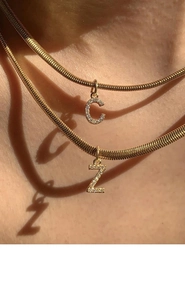 Macro shot of gold snake bone chains with crystal letter C and Z pendants on neck