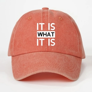 Detailed close-up of 'IT IS WHAT IT IS' text printed on a washed coral baseball cap